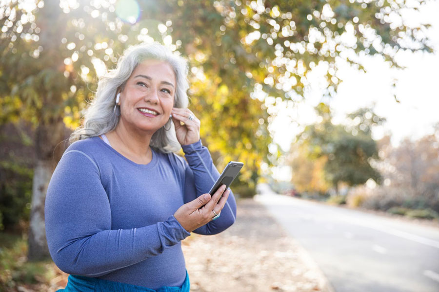 senior woman outside in workout gear, putting in wireless headphones