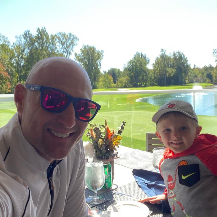 Bobby Petras with his son sitting at tables at golf course club with course in the background.