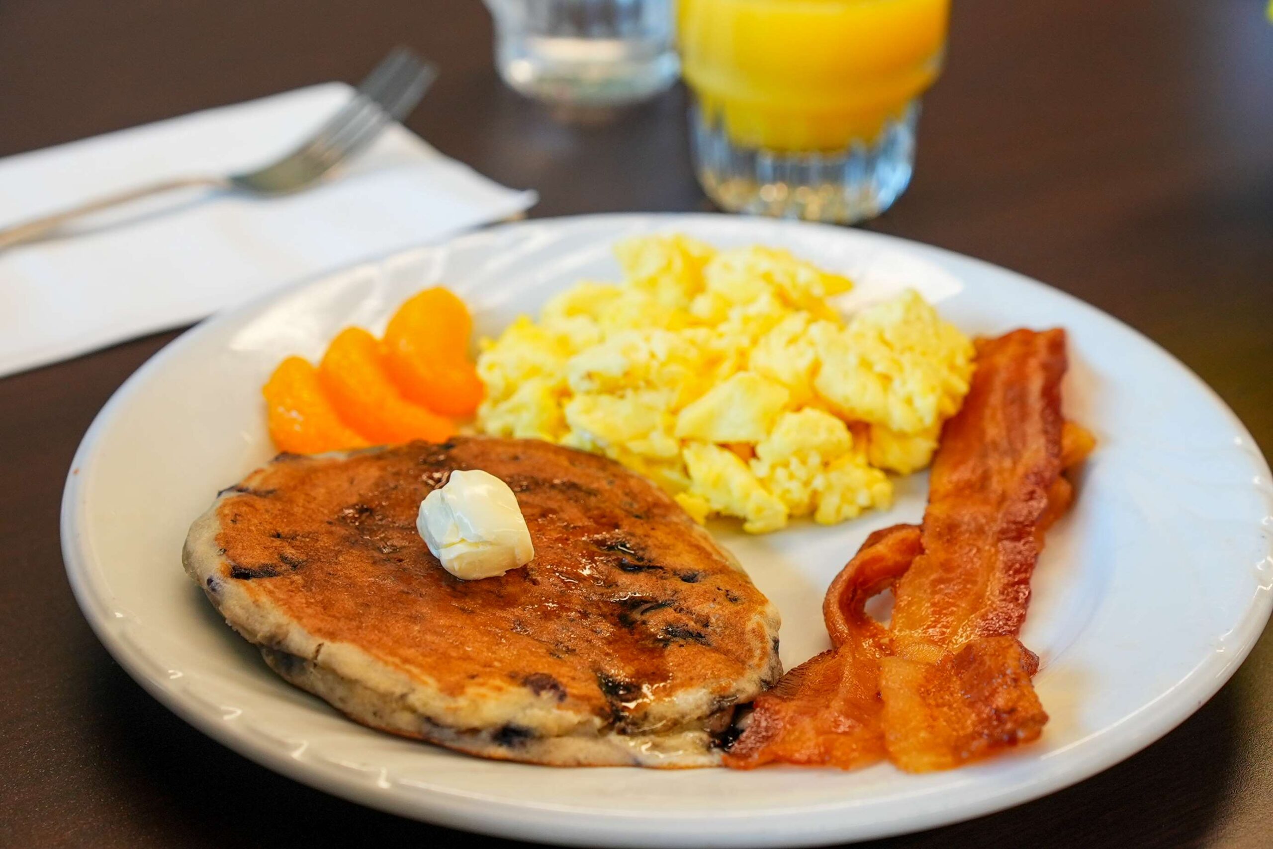 Chocolate chip pancakes, bacon, and eggs with fresh orange slices. Zoomed in.