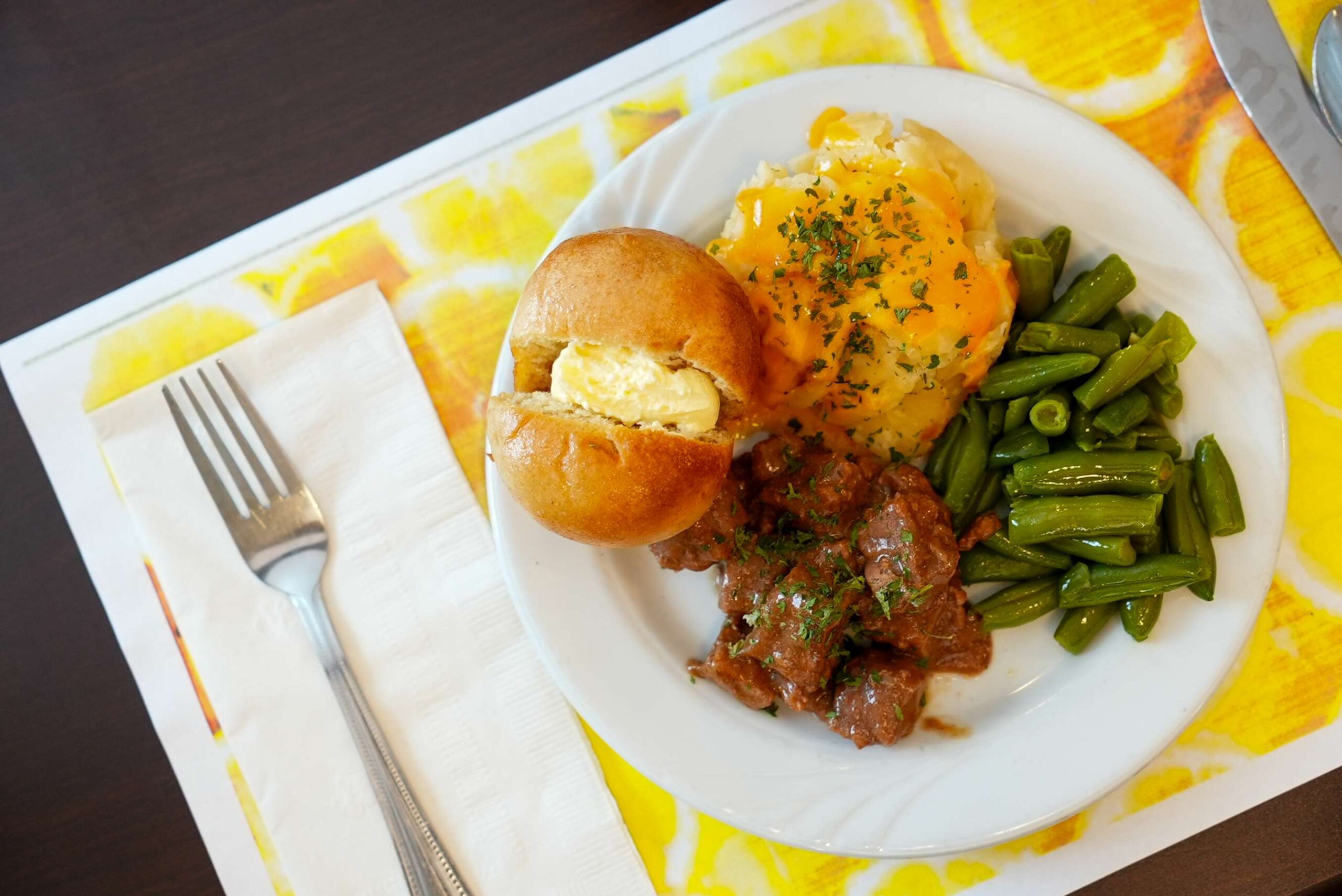 Roast beef, green beans, and potatoes with a buttered roll.