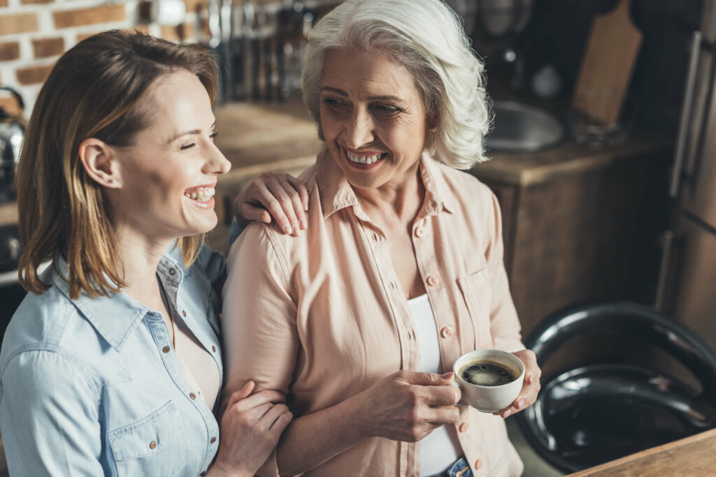 Senior woman drinking coffee with another woman holding her arm