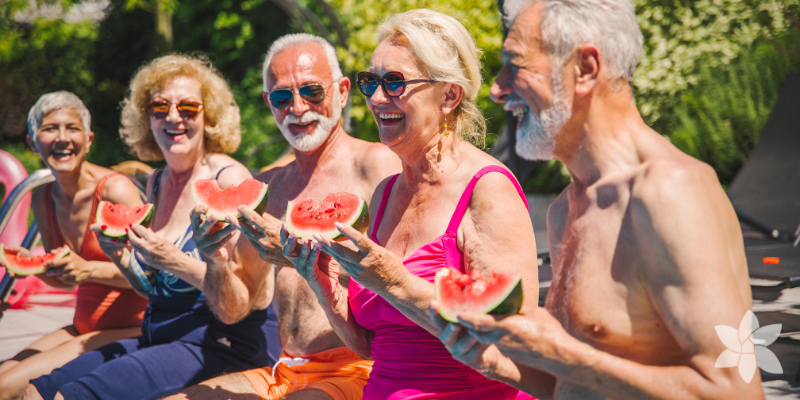 Seniors sitting on the edge of a pool enjoying watermelon