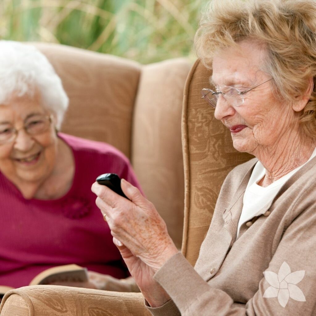 Two senior women sitting in chairs, one reading and the other on her phone