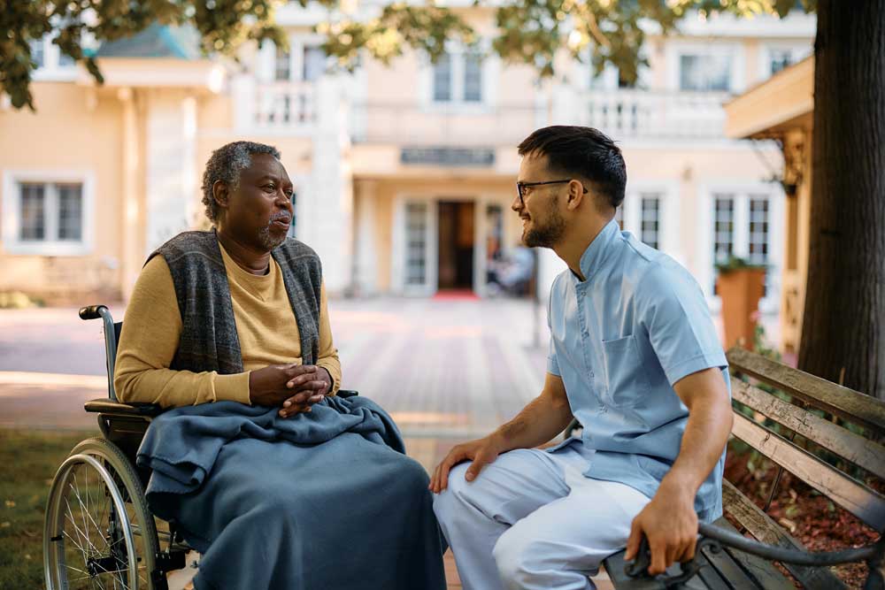 Senior man in a wheelchair outdoors, with a caregiver