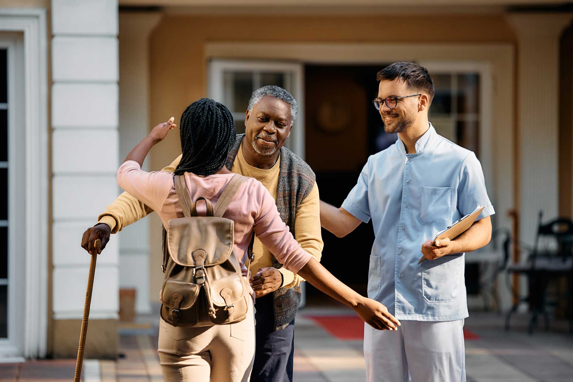 Resident hugs his loved one goodbye with caregiver standing nearby.